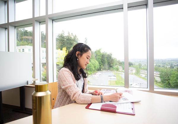 Young woman working at a table beside a window. 