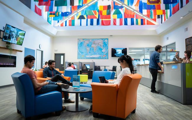 Students sitting together in an indoor space beneath flags of the world